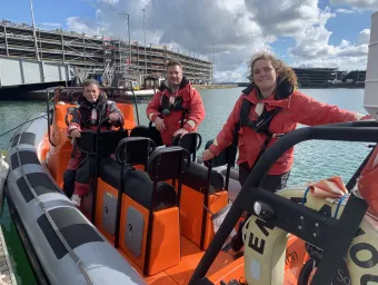 Three instructors standing on a powerboat moored at the quay side. They are all and looking directly at the camera. You can see the multistorey cruise parking building in the background.