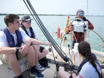 Students sitting on a boat, watching an instructor.