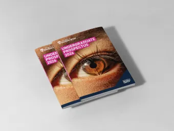 A small stack of university prospectuses on a table. The front cover of the prospectus reads 'Undergraduate Prospectus 2026' and features a close-up image of an eye, with the reflection of an open book.