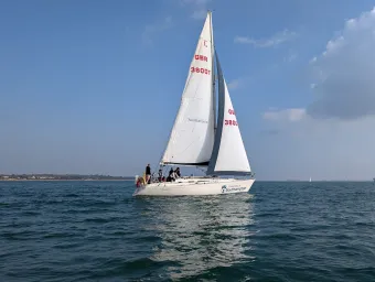 A yacht with 2 sails up and course participants sailing along the coast