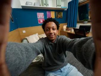 A student taking a selfie while sat on a bed in a university halls of residence.