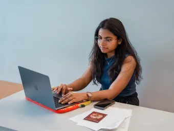A student sat a desk with a laptop, mobile phone, passport and documents.