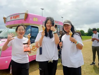 Three students stood holding ice creams, with an ice cream van in the background.