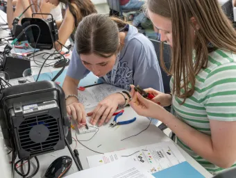 Two young people sitting at a workstation assembling an electronic circuit. 