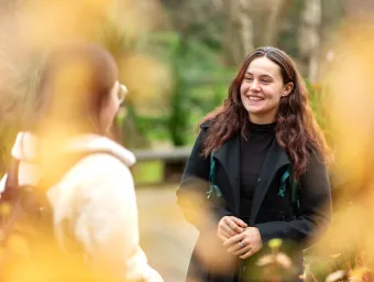 An undergraduate student stood outside talking to someone and smiling.