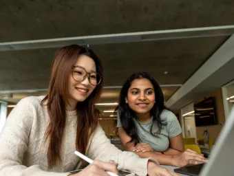 Two international students research courses on a laptop