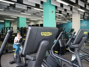 A woman tries out the new cycle machines in the Mayflower gym. She is surrounded by rows of brand new equipment in a spacious hall