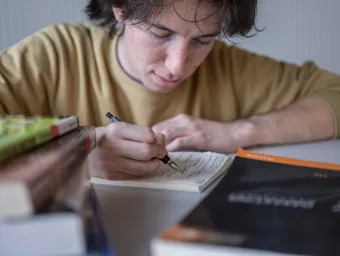 A student leans over a notebook where he writes down questions to ask later