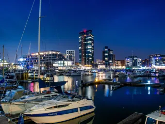 Boats moored at Southampton Marina with illuminated waterfront buildings reflected in the harbour at night.