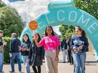 Student ambassador holding a “Follow me” sign leading visitors under a University of Southampton welcome arch.