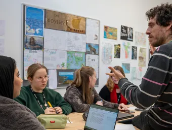 Teacher leading a small classroom discussion with several students seated around a table.