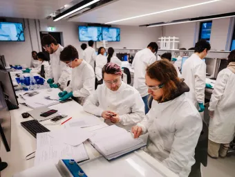 A group praclical taking place in the Biomedical engineering laboratory. Students are wearing white coats and eye protection.