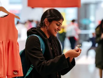 Visitor uses a mobile phone at an indoor event space, with a bright orange dress display and people in the background.