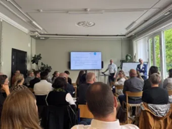 People sitting in front of a screen where a presenter shows a slide on offshore wind topic