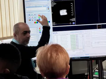 Demonstrator presenting scientific imaging data on a large screen to a group of visitors.