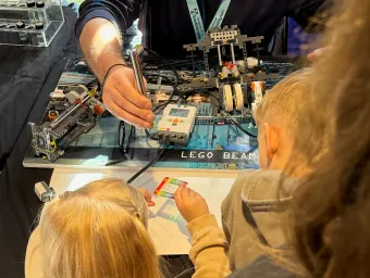 Children take part in a hands-on electronics activity using a LEGO-based machine and sensor equipment at a science demonstration.