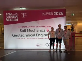 Three IROE researchers standing in front of conference banner