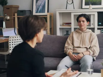 Two people sitting opposite each other talking in a therapy session. 