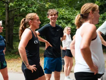 Several people in sportswear stand on a woodland path at the end of a group running session. There are trees and greenery in the background.
