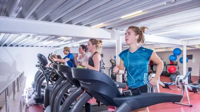 Group of students in gym, running on treadmills surrounded by rowing machines and other gym equipment.