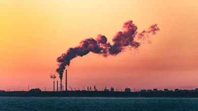 A shot of an industrial shoreline silhouetted at sunset, with smoke from a refinery curling into the sky.