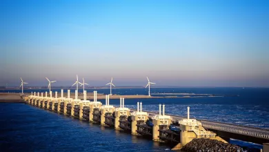 A wide shot of a storm surge barrier, with several wind turbines spinning in the background.