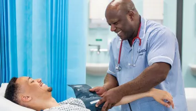 A patient and Southampton student nurse smiling at each other in a hospital room, as the nurse takes the patient's blood pressure.