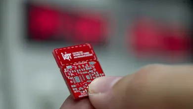Extreme close up of a red internet of things circuit board held between finger and thumb