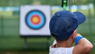 Close up of a child, seen from behind, about to shoot an arrow at an archery target.