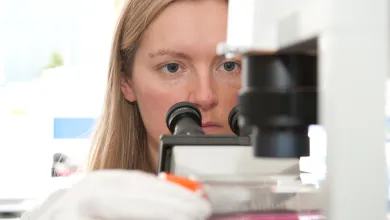 face of a woman placing a sample under a microscope