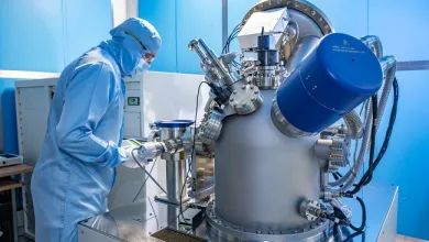 A man in full cleanroom uniform is working with equipment