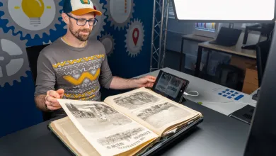 A man digitizes a large illustrated book using a professional overhead camera setup and bright studio lights. The workspace includes advanced imaging equipment, highlighting attention to detail and preservation.