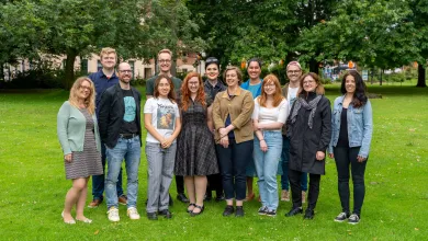A group of people are standing in a park.They are smiling happily at the camera.