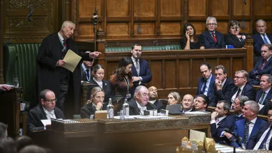 The House of Commons in session. There are multiple people in attendance and someone stood in a black robe speaking.