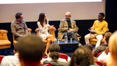 Samuel at a Film Finder event. He's sat with three others in front of an audience. There's a large projection of a presentation behind where they're sat. 
