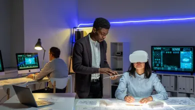 Office setting with a woman in a VR headset at a desk with sketches, accompanied by a man holding a tablet.