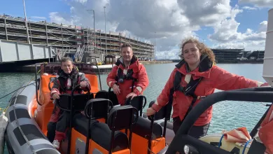 Three instructors standing on a powerboat moored at the quay side. They are all and looking directly at the camera. You can see the multistorey cruise parking building in the background.