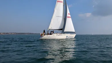 A yacht with 2 sails up and course participants sailing along the coast