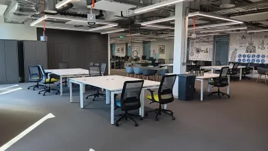 Modern open office space with white desks, black chairs, grey cabinets, and a collaborative area with murals.