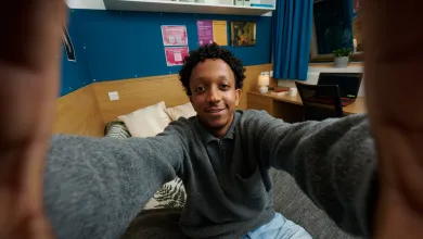 A student taking a selfie while sat on a bed in a university halls of residence.