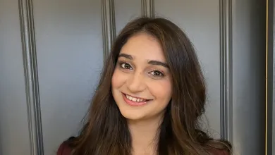 Disha Mehta smiling at the camera, her dark brown hair is long and wavy. It falls over her burgundy jacket.