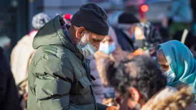 People wearing masks gather outdoors, some handing out fruit during a community food distribution.