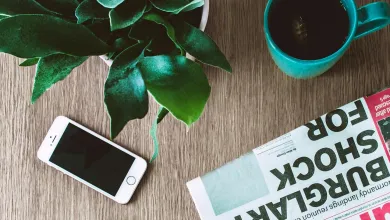table with a mobile phone, plant, beverage in a mug and a newspaper