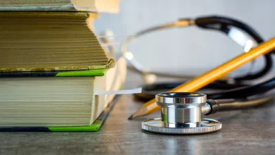 Stack of books with a stethoscope and pencil in front.