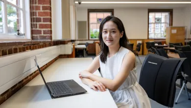 Lin sitting at a desk in an empty classroom. She has a laptop on the desk in front of her, and she's smiling for the camera.