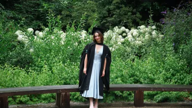 Isabelle, a BSc Pharmacology student, posing for a graduation photo in front of vibrant green foliage and white flowers. 