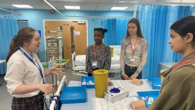 A group of students standing around a hospital bed, listening to a demonstrator.