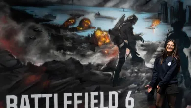 Student standing next to a large promotional Battlefield 6 poster, depicting a soldier walking across burnt landscape.