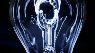 lose-up of an illuminated incandescent light bulb with visible filaments against a dark background.