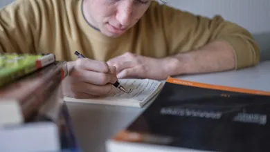 A student leans over a notebook where he writes down questions to ask later
